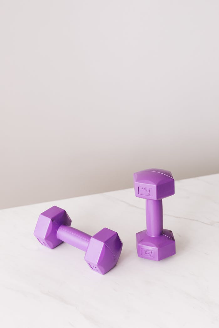 From above of purple dumbbells for fitness training placed on marble surface of table against gray background